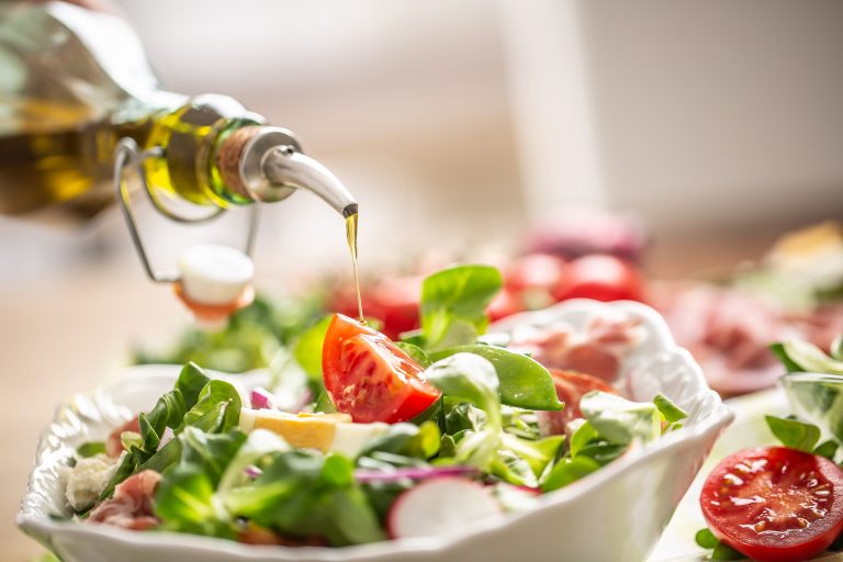 Olivenöl wird über einen frischen, bunten Salat mit Tomaten und Radieschen gegossen.