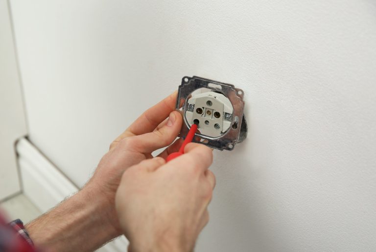 Electrician with screwdriver repairing power socket indoors, closeup
