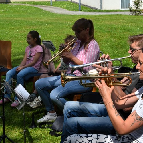 Frauen und Männer des Fanfarenzugs Möhnesee sitzen im Park und spielen für die Bewohnerinnen.