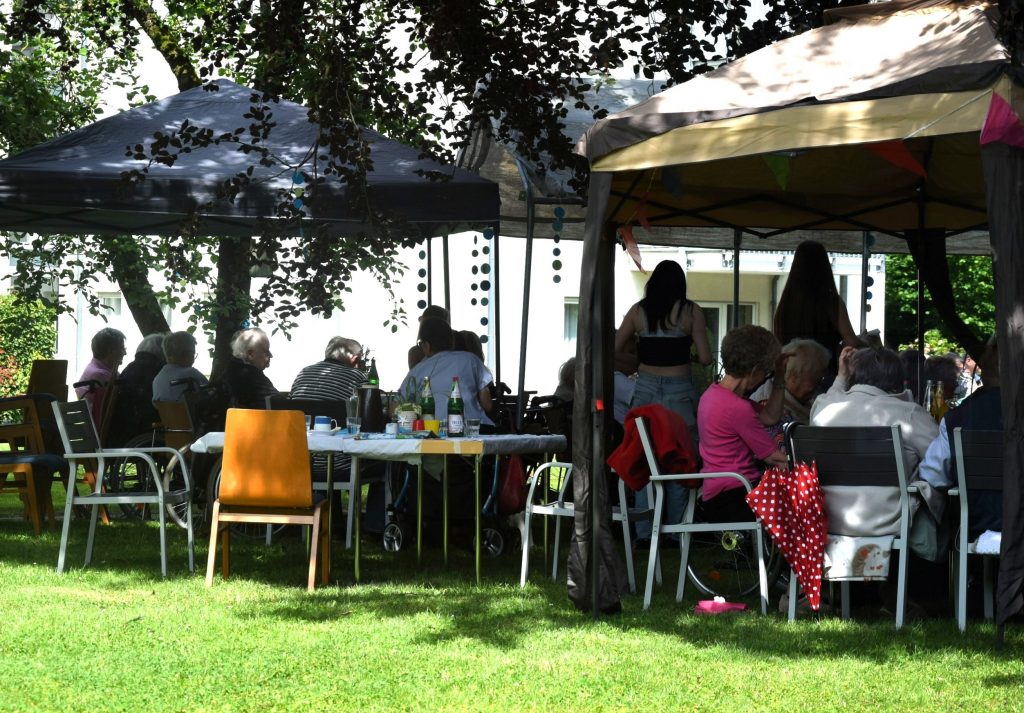Bewohnerinnen und Angehörige sitzen im Schatten von Bäumen im Park des Lina-Oberbäumer-Hauses.
